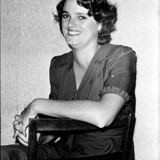Young woman smiling in vintage-style dress, seated.