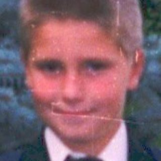 Young boy in formal attire holding bouquet outdoors.
