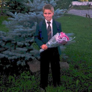 Young boy in formal attire holding bouquet outdoors.