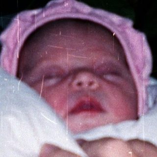 Newborn baby wrapped in blanket, being held outdoors at night.