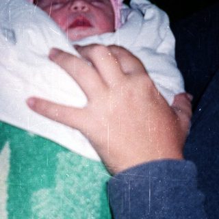 Newborn baby wrapped in blanket, being held outdoors at night.