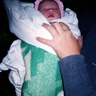 Newborn baby wrapped in blanket, being held outdoors at night.