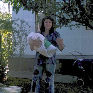 Woman holding baby, smiling outdoors with stroller.
