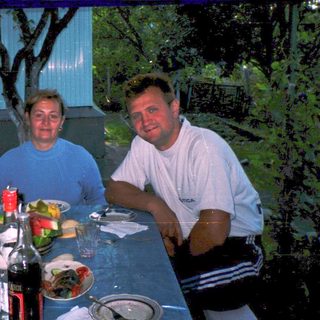 Three people dining outdoors at a table with food and drinks.