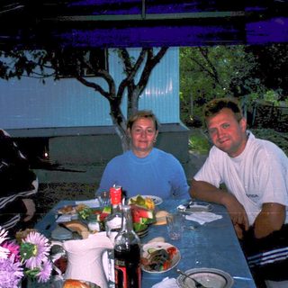 Three people dining outdoors at a table with food and drinks.
