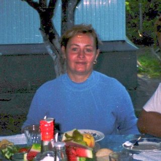 Three people dining outdoors at a table with food and drinks.
