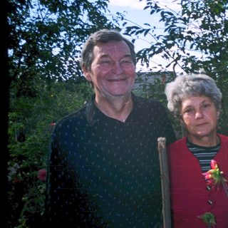 Three adults posing outdoors near greenery.