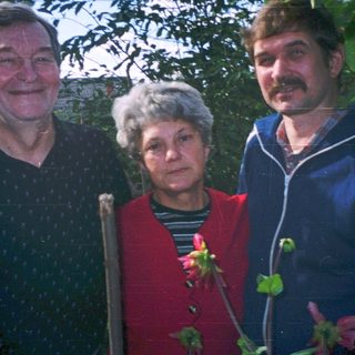 Three adults posing outdoors near greenery.