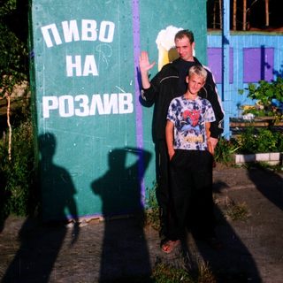 Two men pose near a green wall advertising "beer for pouring."