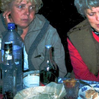 Three people gathered indoors, eating and drinking.