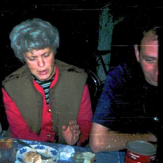 Three people gathered indoors, eating and drinking.