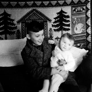 Young boy holding smiling baby indoors.