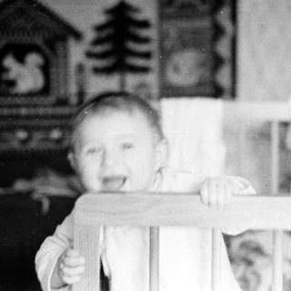 Baby peeking over crib railing indoors.