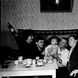 Family gathering with baby indoors, mid-20th century.