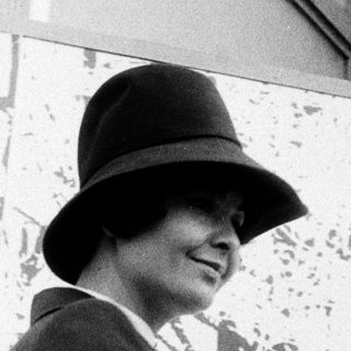 Elegant woman wearing hat and coat, smiling outdoors.