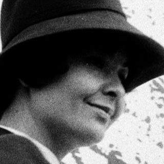Elegant woman wearing hat and coat, smiling outdoors.