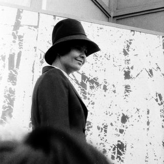 Elegant woman wearing hat and coat, smiling outdoors.