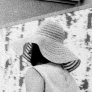 Woman in hat and striped dress walking indoors.