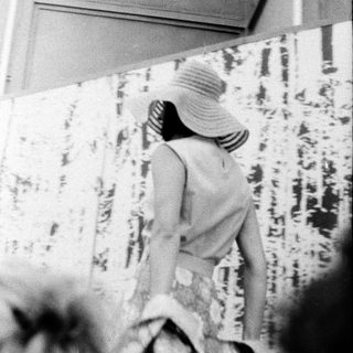 Woman in hat and striped dress walking indoors.