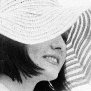 Woman in wide-brim hat under canopy.
