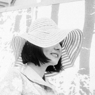 Woman in wide-brim hat under canopy.