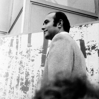 Man in coat indoors, looking upward.