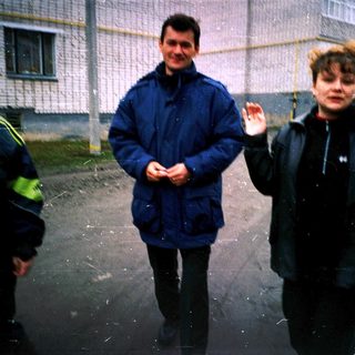 Three people standing outside in light rain.
