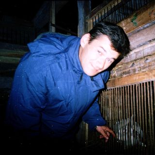 Man standing in dark, rainy area near wooden fence.