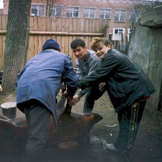 People lifting a heavy metal object outdoors.