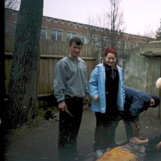 Four people posing outdoors in wet, muddy area.