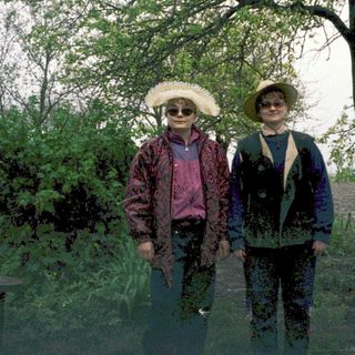 Two people wearing hats and rain gear standing outdoors in wet park area.