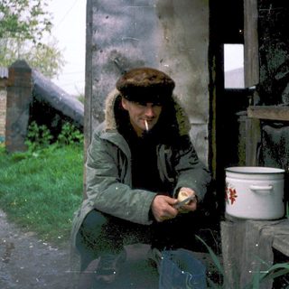 Man smoking outdoors near rustic water container.