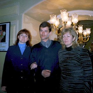 Three people posing indoors near chandeliers.