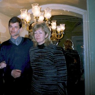 Three people posing indoors near chandeliers.