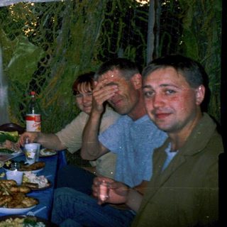 Group of men enjoying meal outdoors under tent.