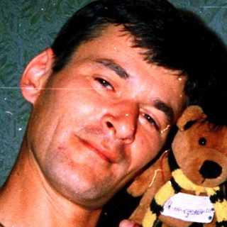 Showering man holding wet teddy bear.