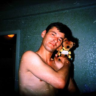 Showering man holding wet teddy bear.