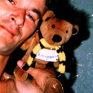 Showering man holding wet teddy bear.