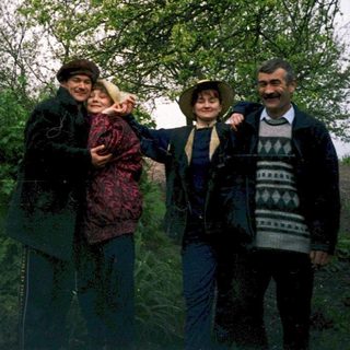 Four people posing outdoors near a wooden structure.