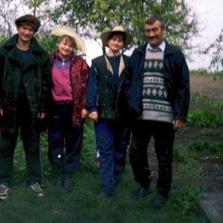 Four people posing outdoors in a rural setting.