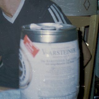 Two people sitting indoors, drinking near a beer keg.