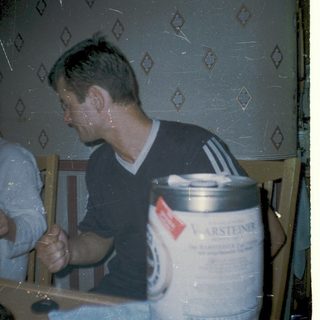Two people sitting indoors, drinking near a beer keg.