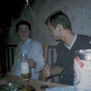 Two people sitting indoors, drinking near a beer keg.