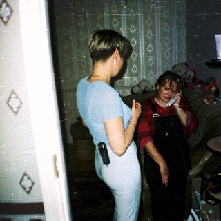 Two women in bathroom, one talking on phone.