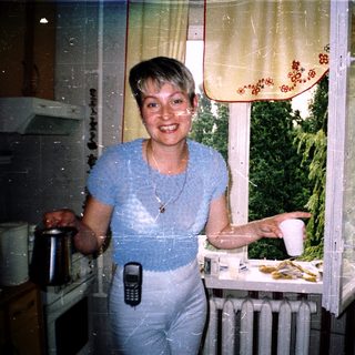 Woman smiling by kitchen window holding cup.