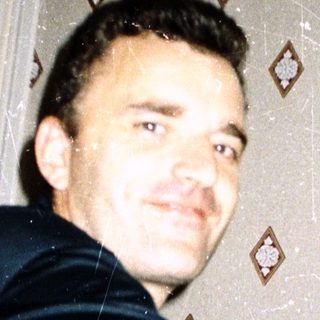 Man smiling indoors near kitchen counter.