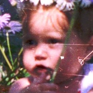 A child peeking out of a flower-filled basket surrounded by greenery.