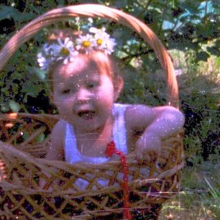 Baby sitting in a wicker basket outdoors.