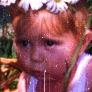 Child sitting in flower-filled basket surrounded by blooming flowers.