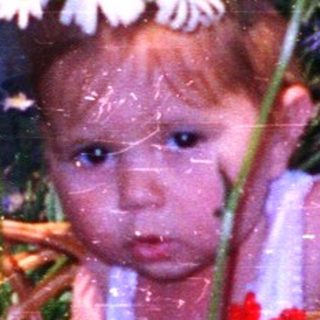 Baby in flower-wreathed basket surrounded by wildflowers.